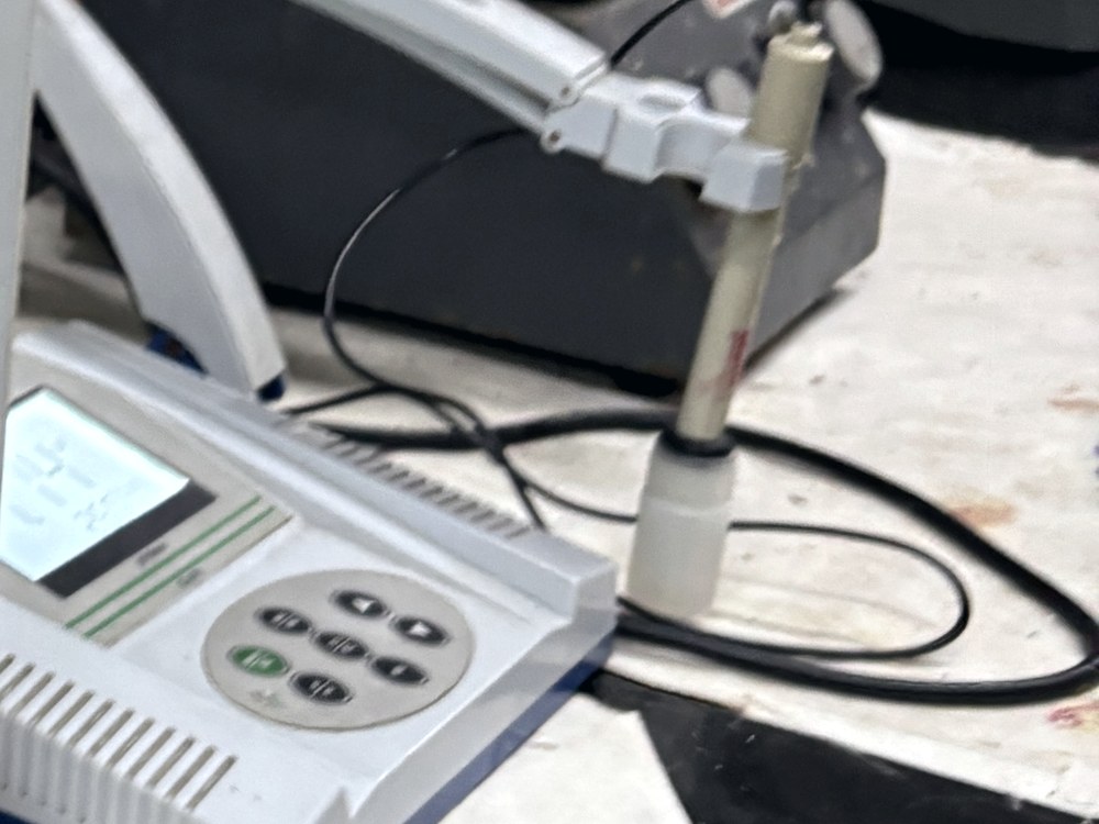 A bench meter with its probe clamped in a stand, cables coiled across a stained worktop.
