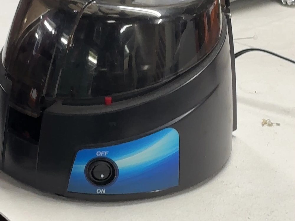 A small benchtop centrifuge, lid closed, its power switch set to off.